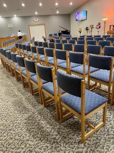 Rows of blue upholstered chairs in a large room, likely a chapel. A piano and screen are visible.