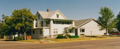 A two-story white building with green awnings and a wheelchair ramp on a sunny day.