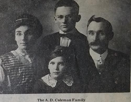 Family portrait: four people in formal attire.  Man with mustache, woman with headband, young man with glasses, and a woman in the center.