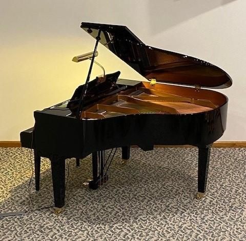 Black grand piano, partially open, indoors, lit by a lamp.
