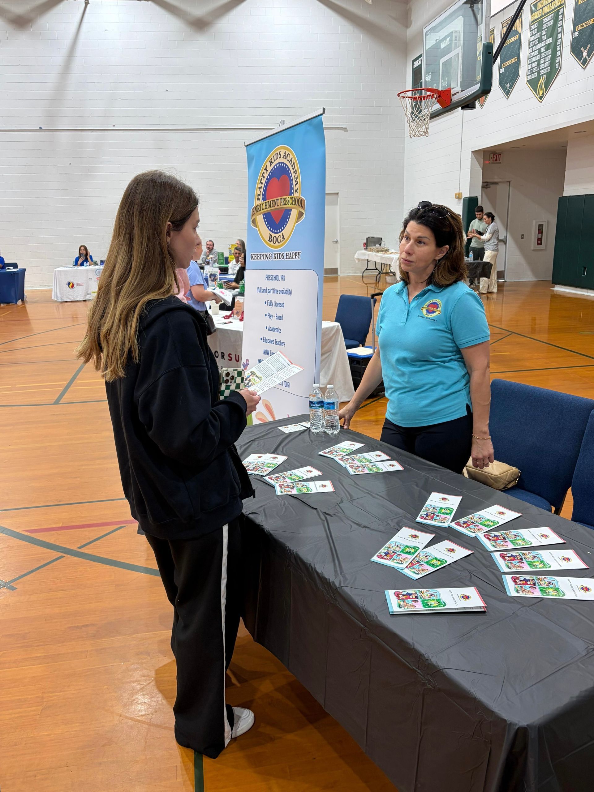 Two people at a table with brochures in a gymnasium booth at an event
