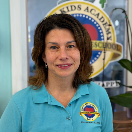 Woman in turquoise polo smiling in front of a Kids Academy School logo