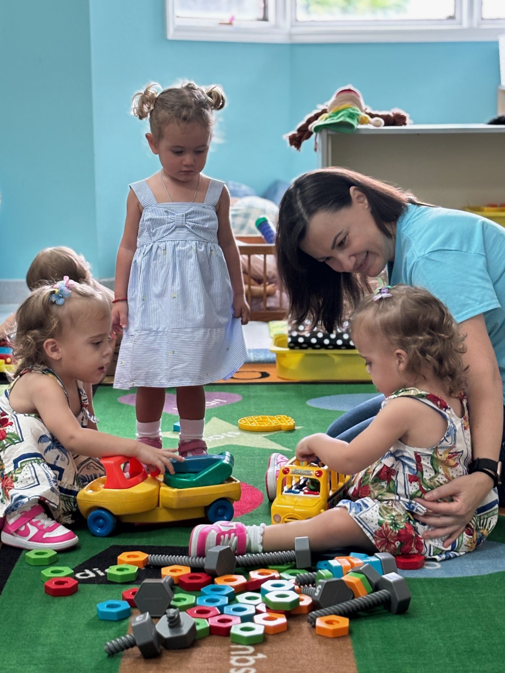 Children and adult play with toys in a classroom.