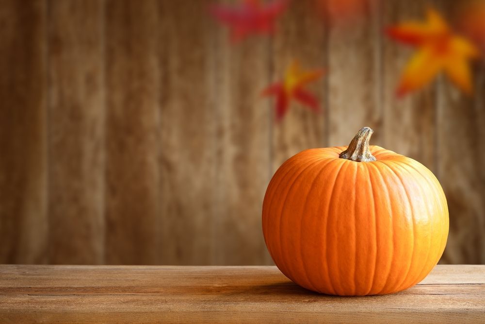 Orange pumpkin on a wooden surface against a blurred wooden background with fall leaves.