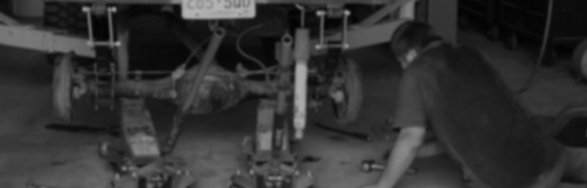 A person working on the rear axle of a vehicle. The axle is suspended in a garage. | Performance Automotive Repair