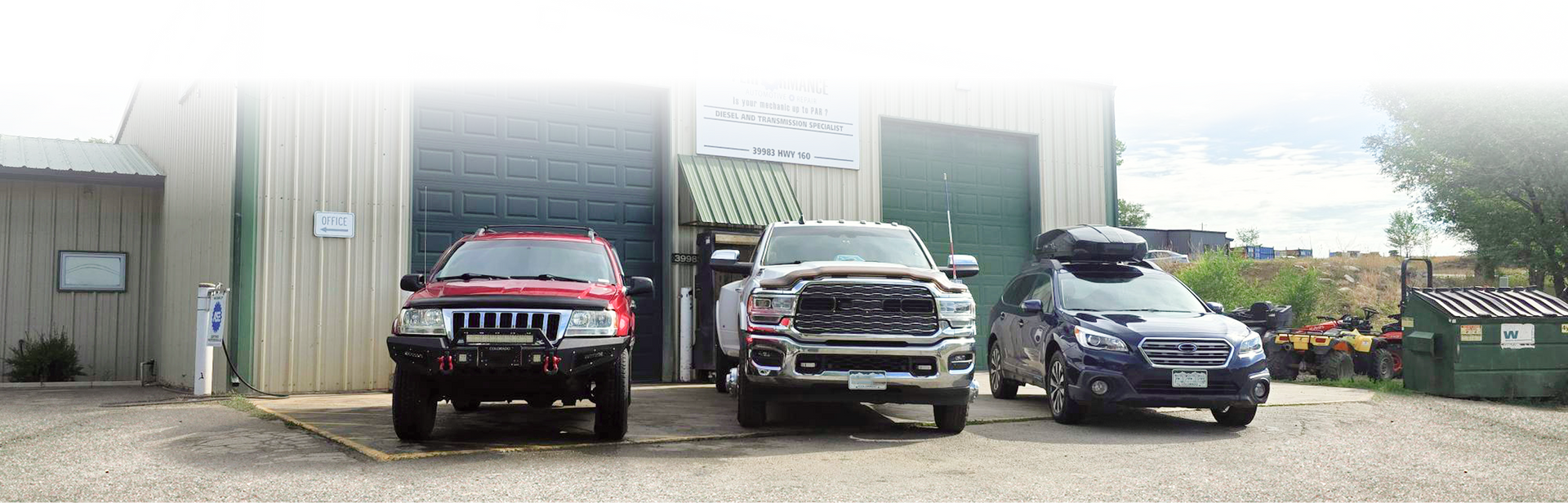 Three vehicles parked in front of a metal warehouse building, with a red SUV, a silver pickup, and a blue car. | Performance Automotive Repair