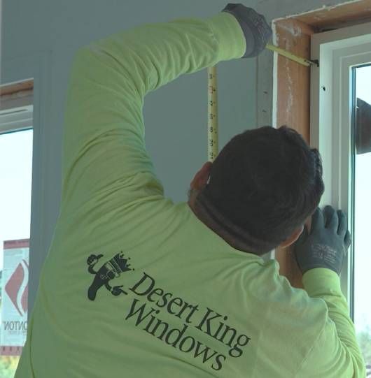 Worker in neon green shirt measuring a window frame with a tape measure