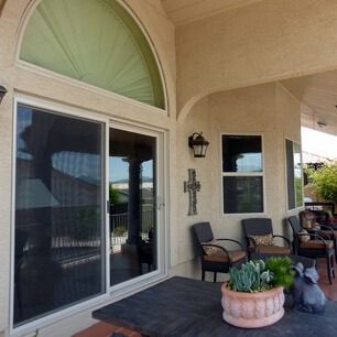 Patio with sliding glass door, chairs, wall cross, and potted plants under an arched awning