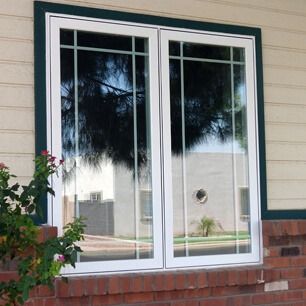 White-framed sliding glass door in a brick wall, reflecting a tree and outdoor street scene.