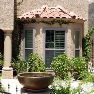 Courtyard with terracotta roof, stucco walls, window shutters, and a stone fountain surrounded by greenery