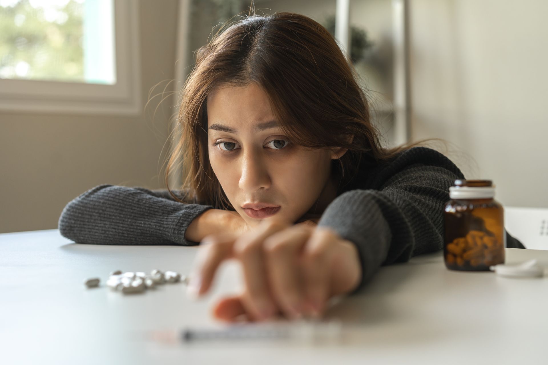 A woman sits at a table with a bottle of pills and a syringe.