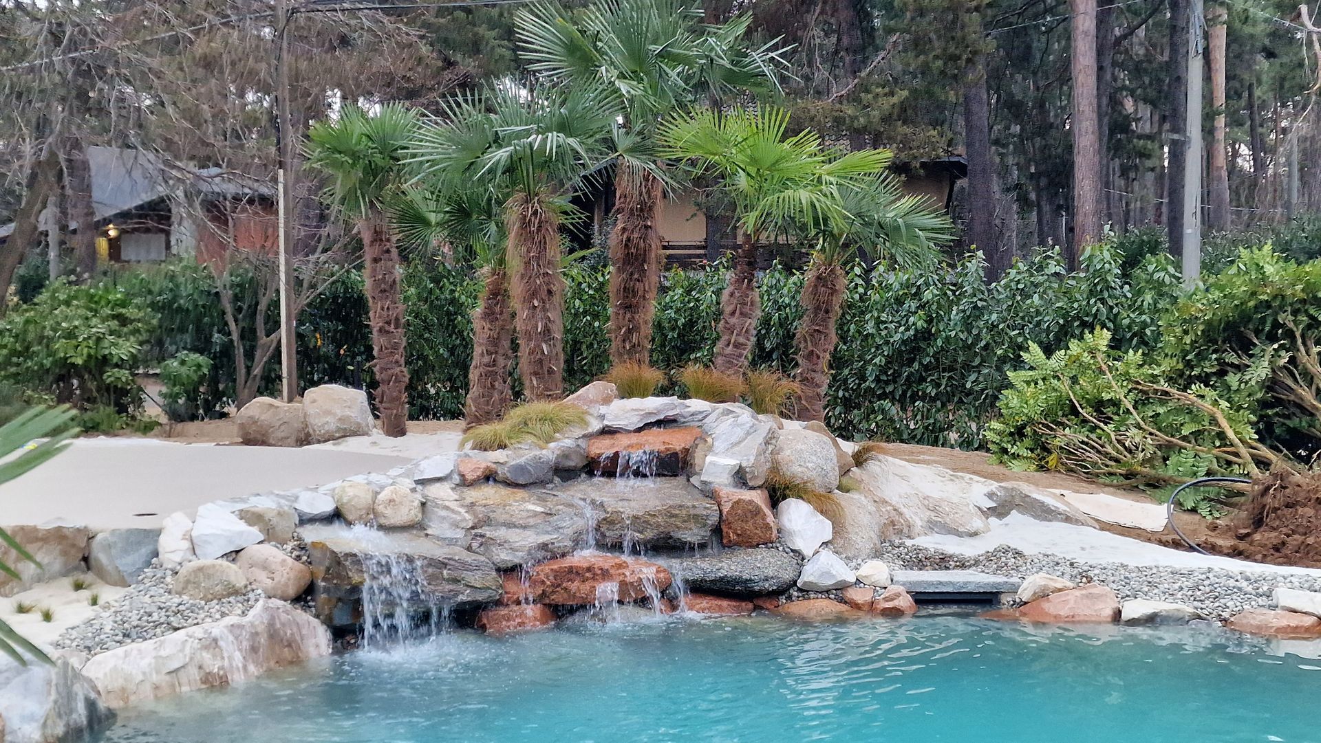 Cascata rocciosa che si riversa in una piscina turchese tra palme e vegetazione lussureggiante.