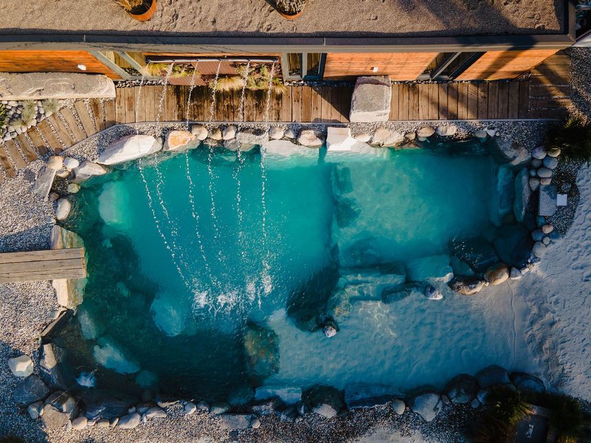 Veduta aerea di una piscina termale turchese accanto a una passerella di legno e a pareti rocciose.