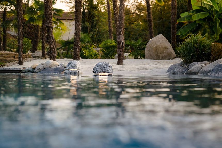 Tranquilla piscina del resort con acqua cristallina, rocce bianche, palme e una calda luce serale.