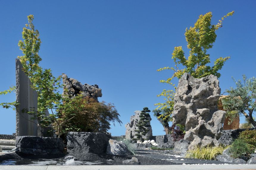 Sculture da giardino in pietra all'aperto con piante verdi sotto un cielo azzurro limpido.