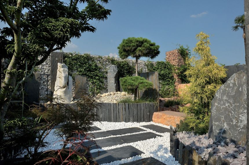 Giardino paesaggistico moderno con scalini in pietra, alberi potati e muri in pietra esposti alla luce del sole.
