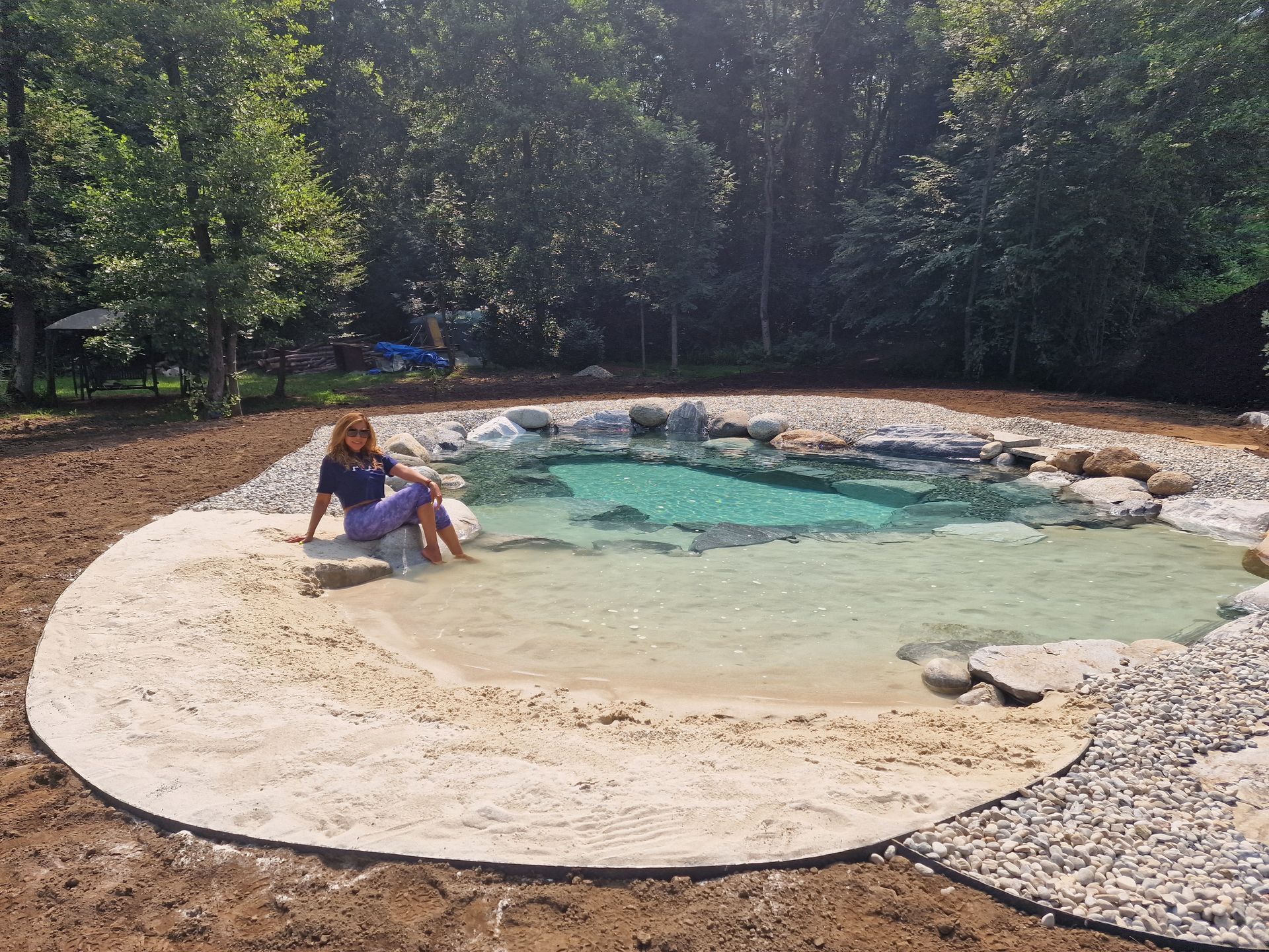 Una persona seduta accanto a una piccola piscina turchese in un'area boschiva all'aperto.