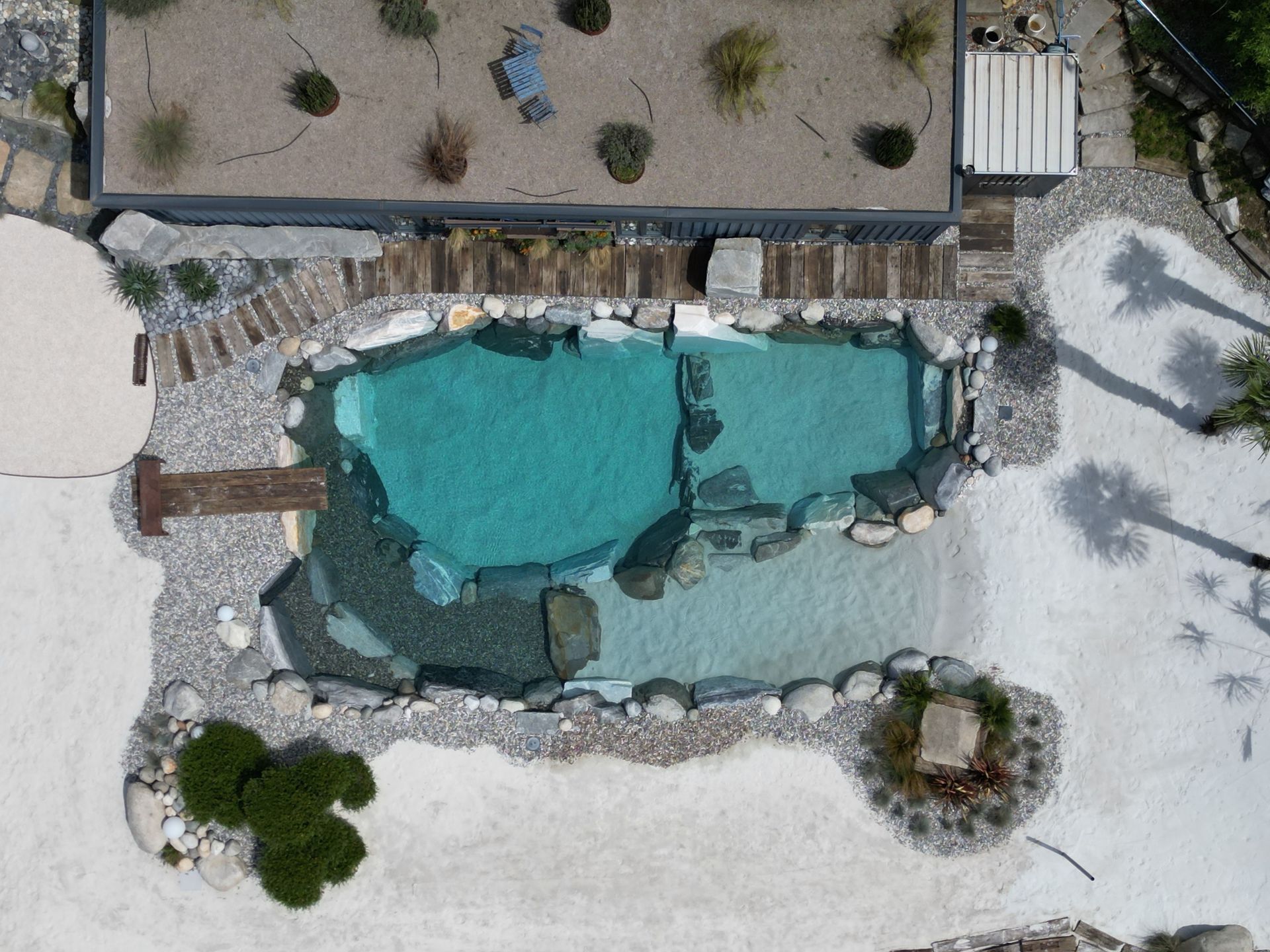 Veduta aerea di una piscina turchese con bordo in pietra in un paesaggio desertico.