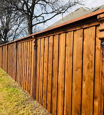 A wooden fence is sitting next to a grassy field in front of a house.