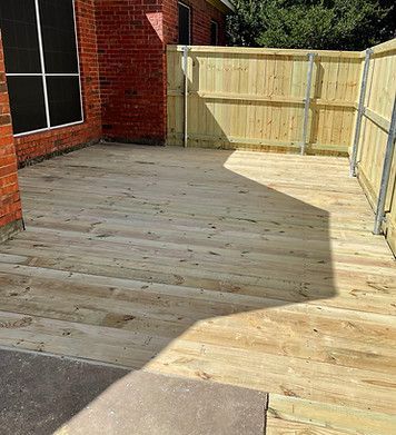 A wooden deck with a wooden fence and a brick building in the background.