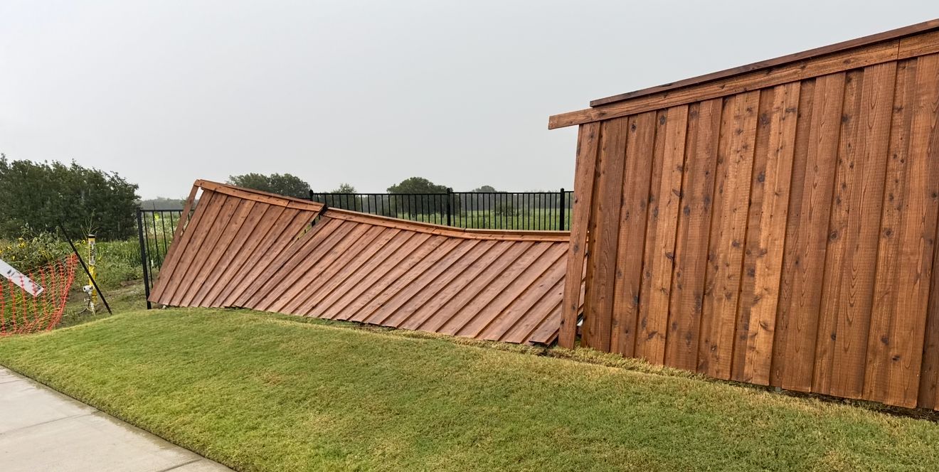 Collapsed wooden fence beside a grassy path, with a standing brown shed in the background.