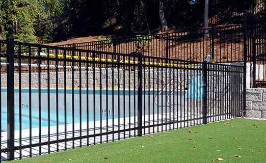 Black metal fence beside a blue swimming pool and grassy lawn outdoors