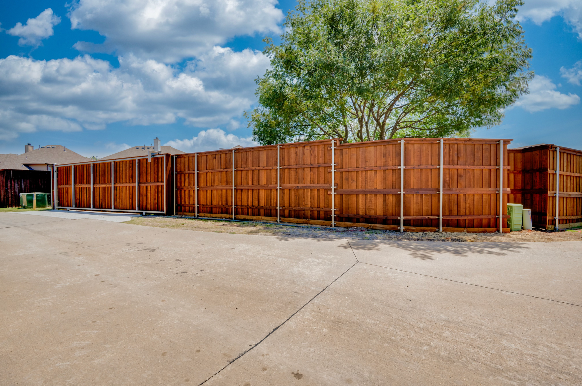 Long wooden fence bordering a dirt lot under a blue sky with clouds