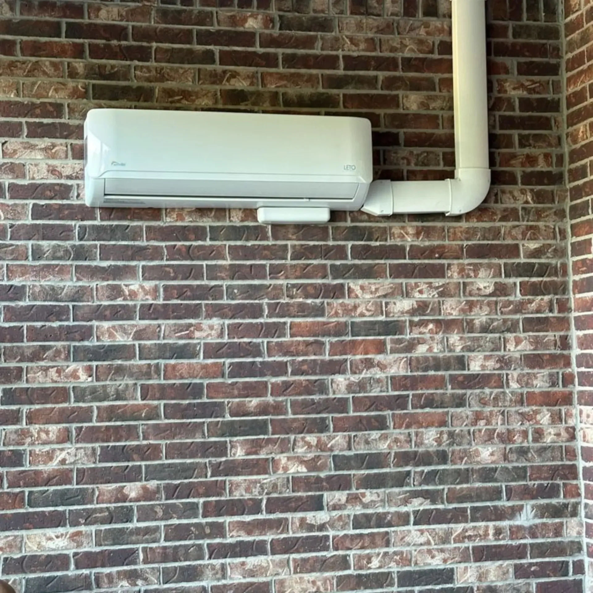 Finnegan’s Heating Air Conditioning - A white air conditioner is mounted on a brick wall.