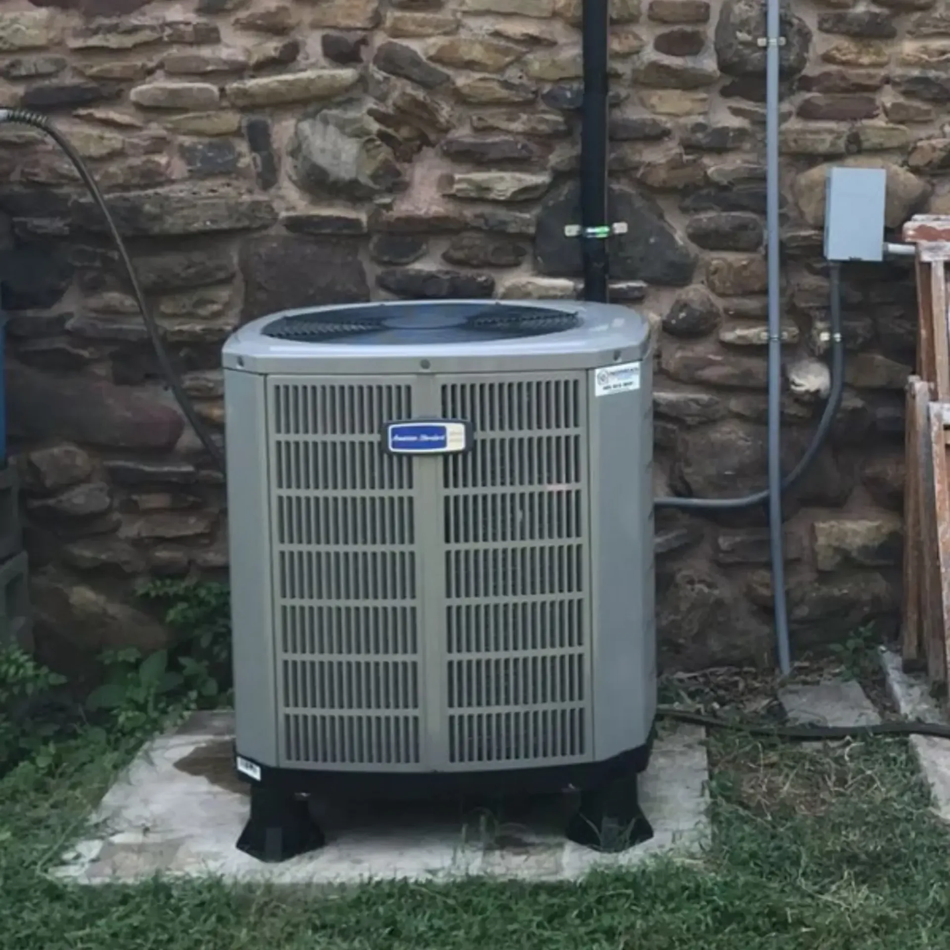 Finnegan’s Heating Air Conditioning - A gray air conditioner is sitting in front of a stone wall.