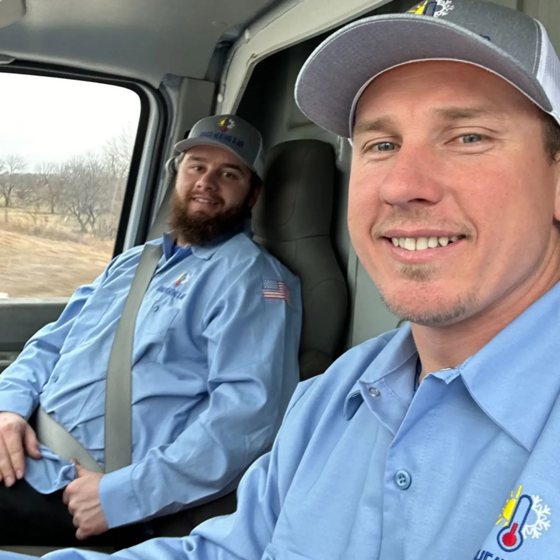 Finnegan’s Heating Air Conditioning - Two men wearing blue shirts and hats are sitting in a car