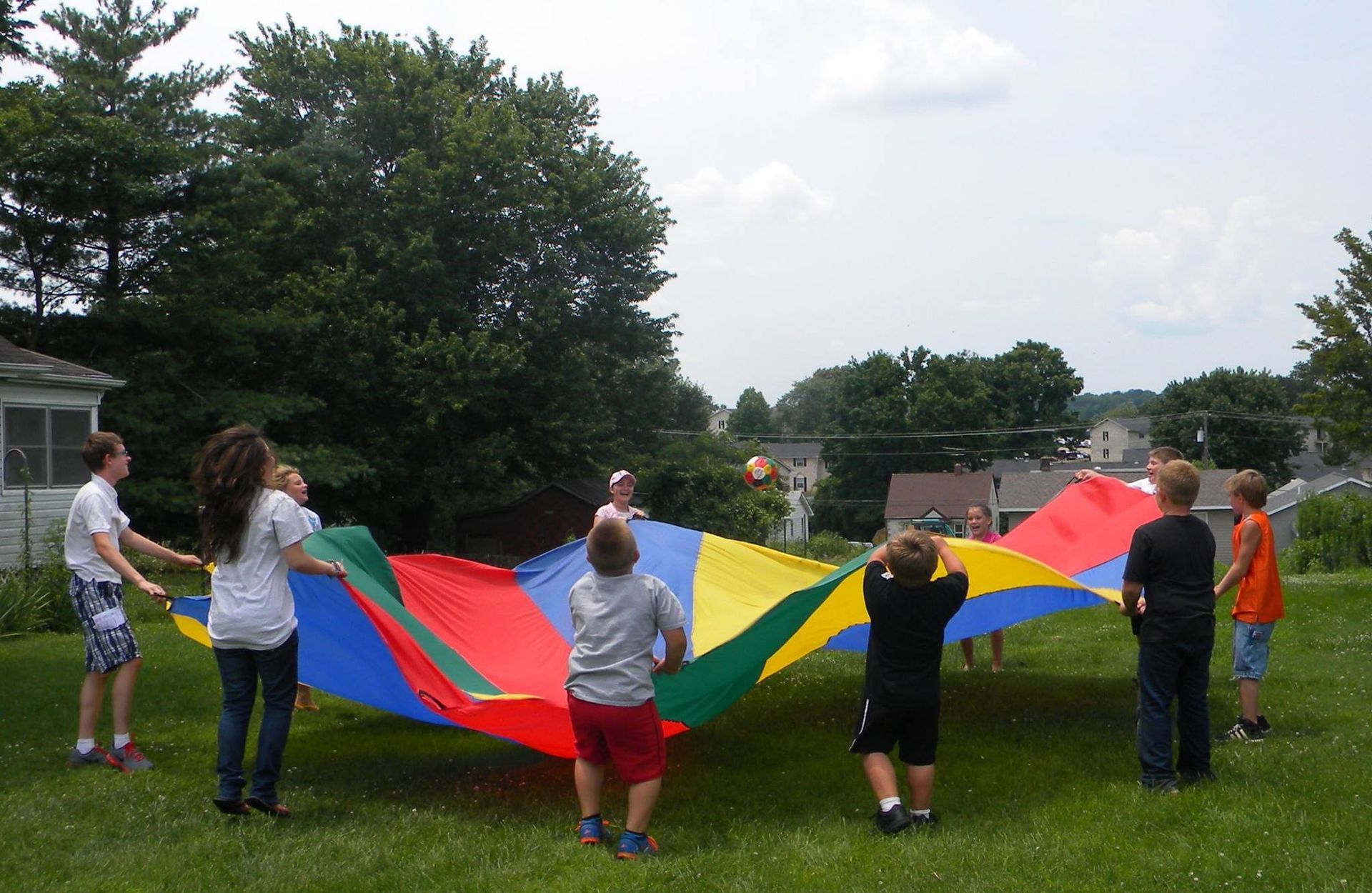 Children playing with a colorful parachute on a grassy lawn.