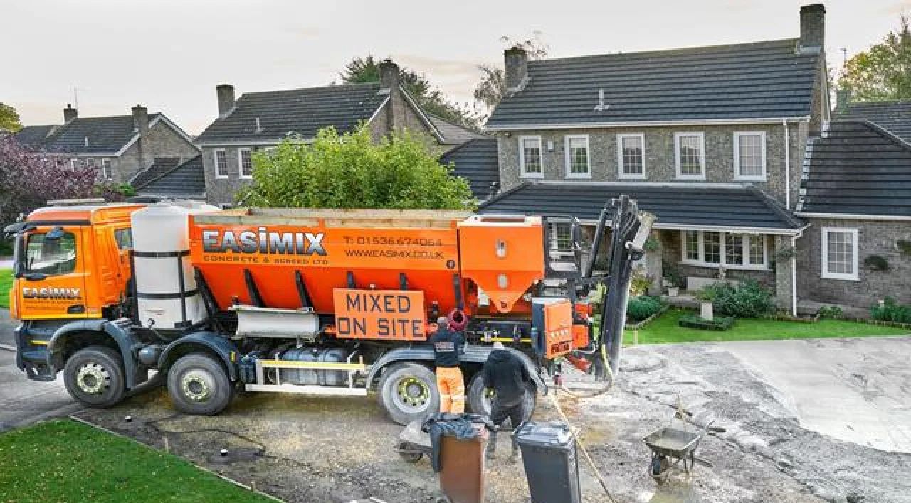 Orange concrete mixer truck at a house under construction, with workers and debris in a residential driveway
