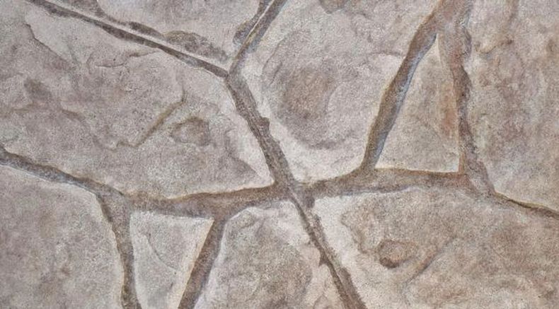 Close-up of a gray-beige stone wall with irregular, cracked mosaic-like patterns