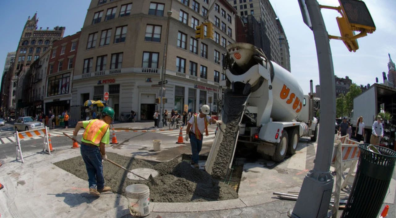 Construction worker near a concrete truck pouring pavement at a city intersection