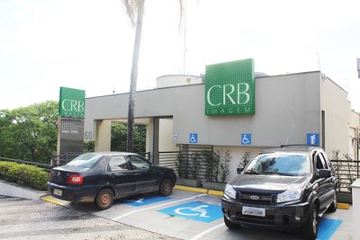 Exterior de um prédio com vagas de estacionamento acessíveis. Carro preto e SUV estacionados. Placa verde com