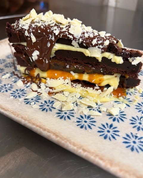 Torta a strati di cioccolato con ripieno al caramello, servita su un piatto decorato e guarnita con scaglie di cocco.