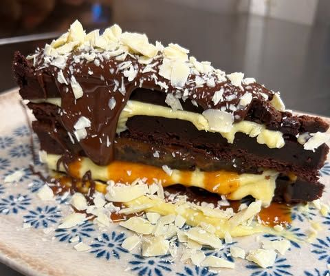 Torta a strati di cioccolato con ripieno al caramello, servita su un piatto decorato e guarnita con scaglie di cocco.