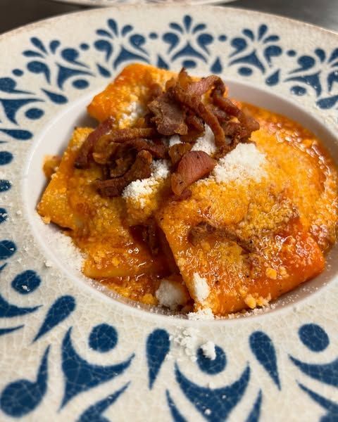 Piatto di ravioli all'arancia con formaggio grattugiato e cipolle fritte, serviti su un piatto decorato in bianco e blu.