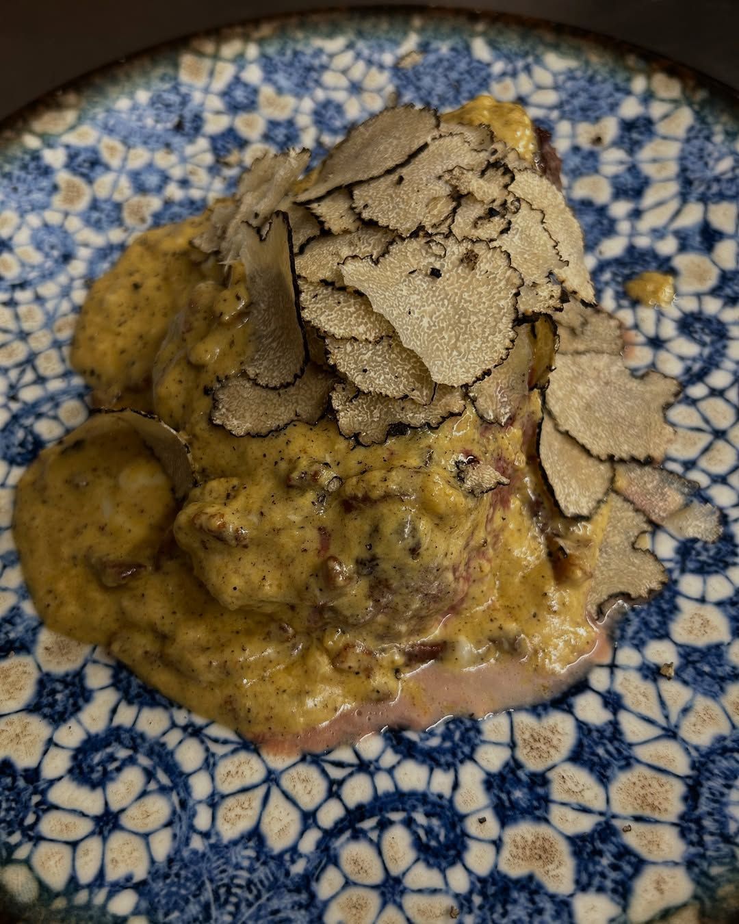 Un piatto impiattato con scaglie di tartufo su un piatto decorato in blu e bianco.