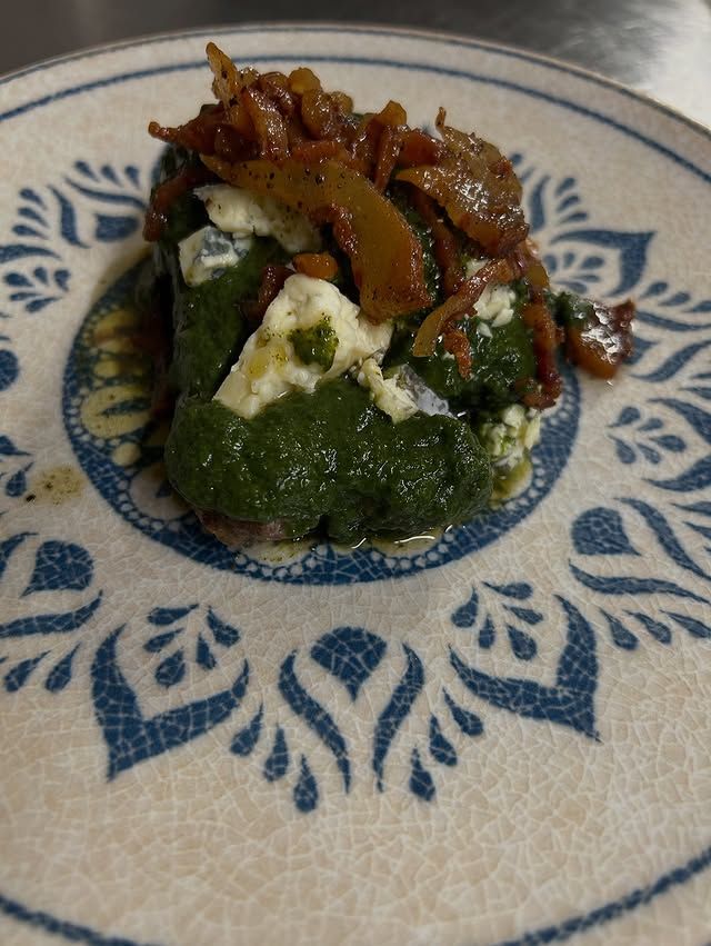Piccola porzione di cibo verde e bianco guarnita con cipolle caramellate su un piatto decorato in blu e bianco.