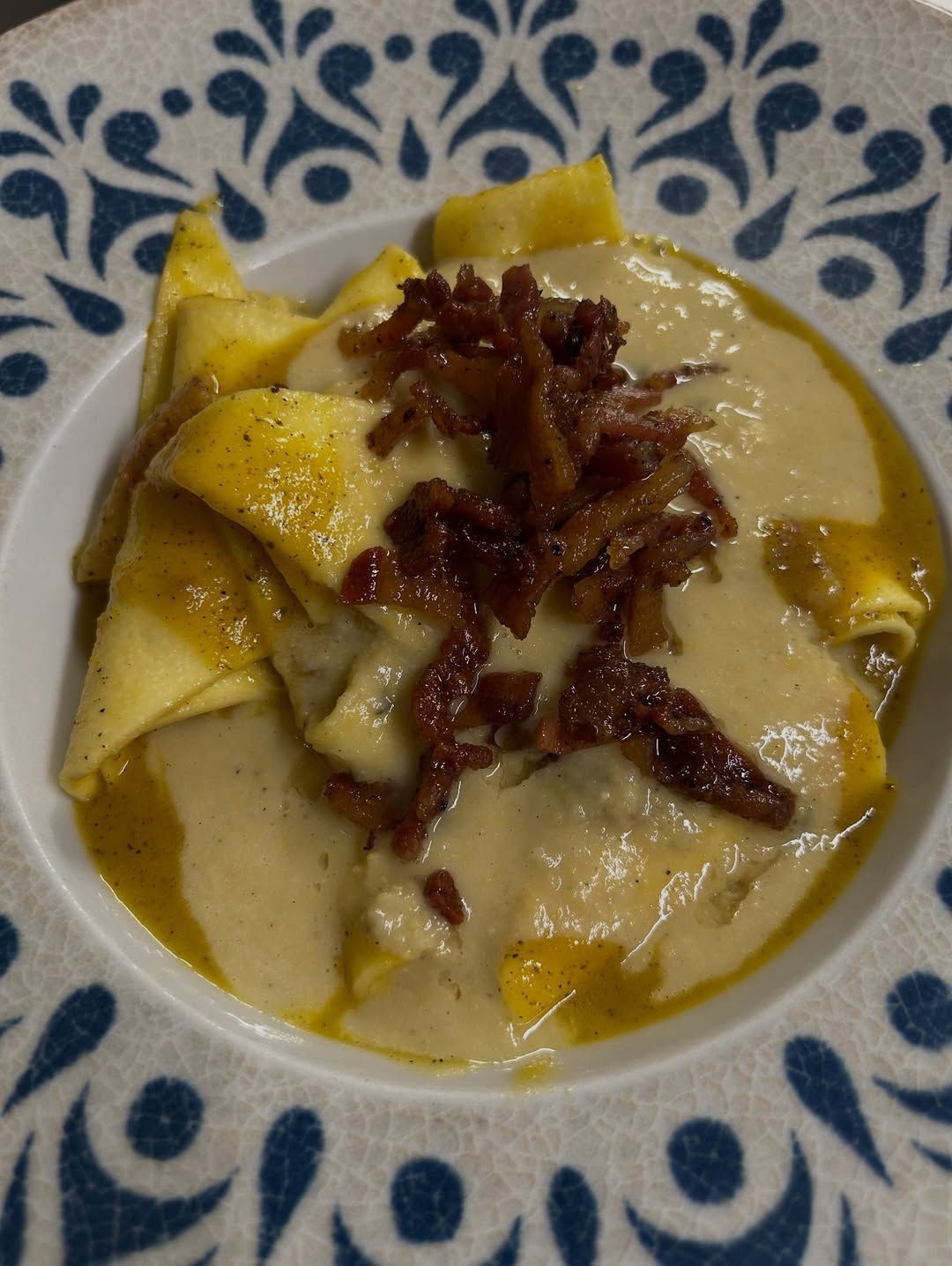 Piatto di crêpes gialle condite con salsa cremosa e pancetta croccante su un piatto blu a fiori.