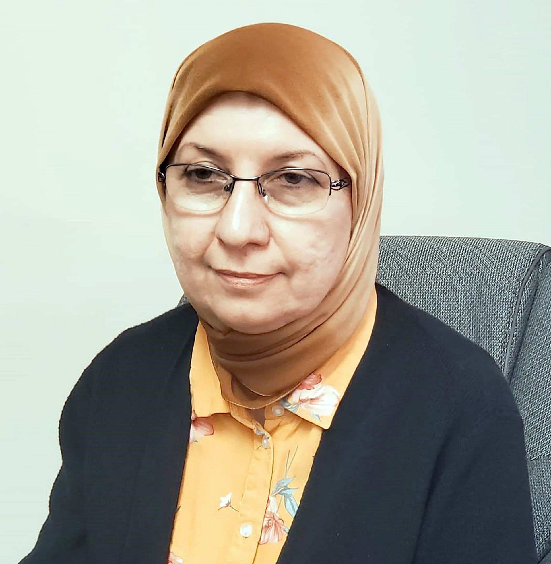 A woman wearing glasses and a hijab is sitting in a chair