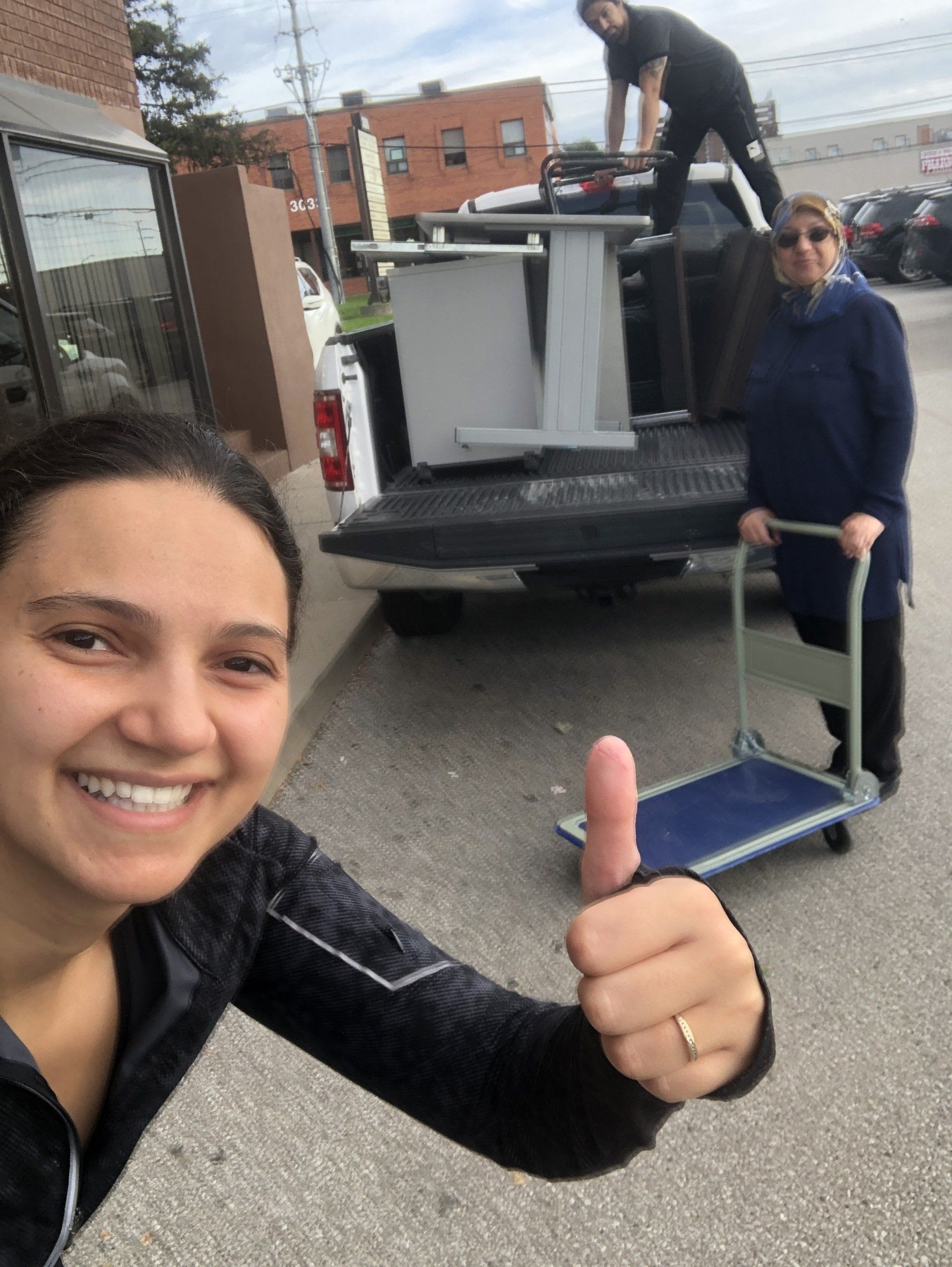 A woman is giving a thumbs up in front of a truck.