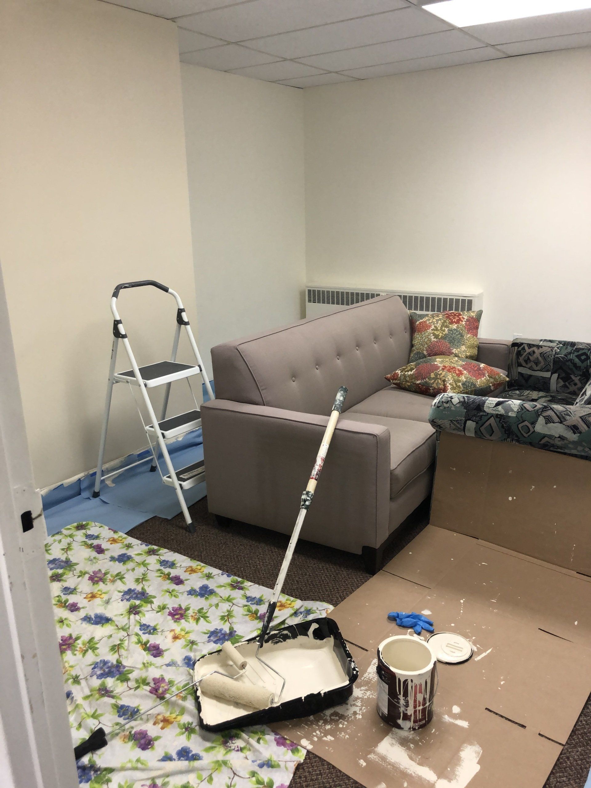 A living room with a couch , chair , and ladder being painted.