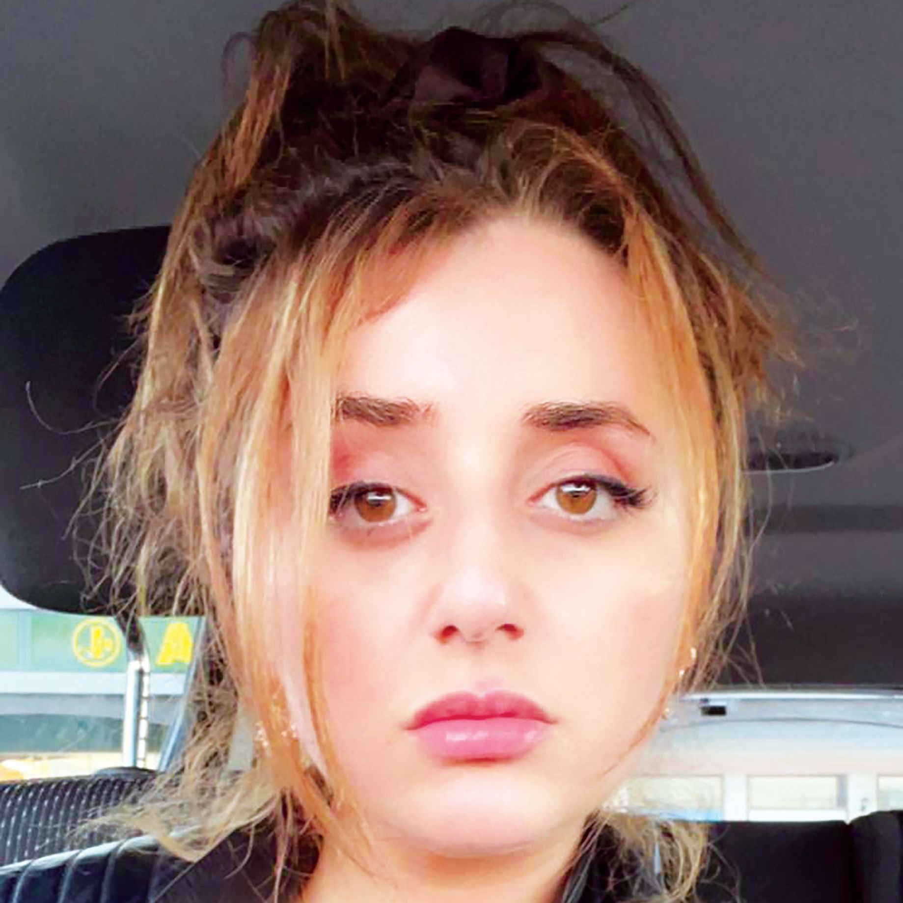 A woman is sitting in a car and looking at the camera.