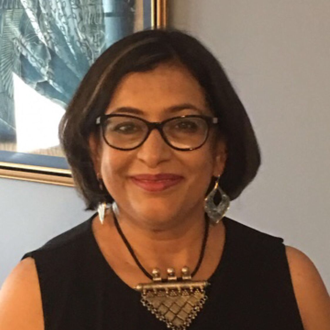 A woman wearing glasses and a necklace smiles for the camera