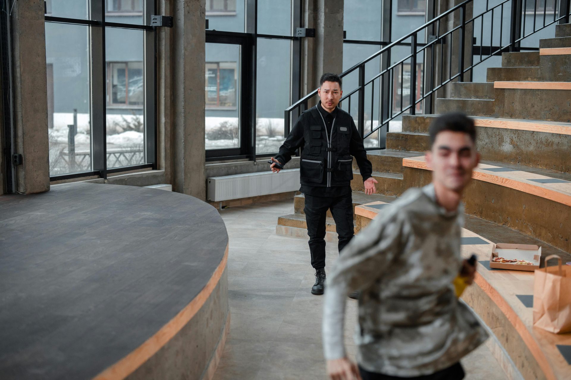 Man in black approaches a running person in a modern building.