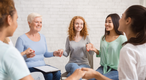 A group of women are sitting in a circle holding hands.