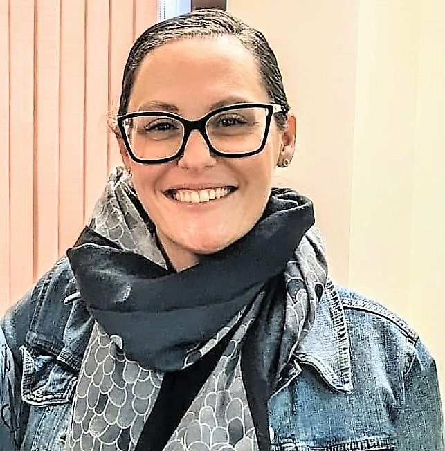 A woman wearing glasses and a scarf is smiling for the camera.