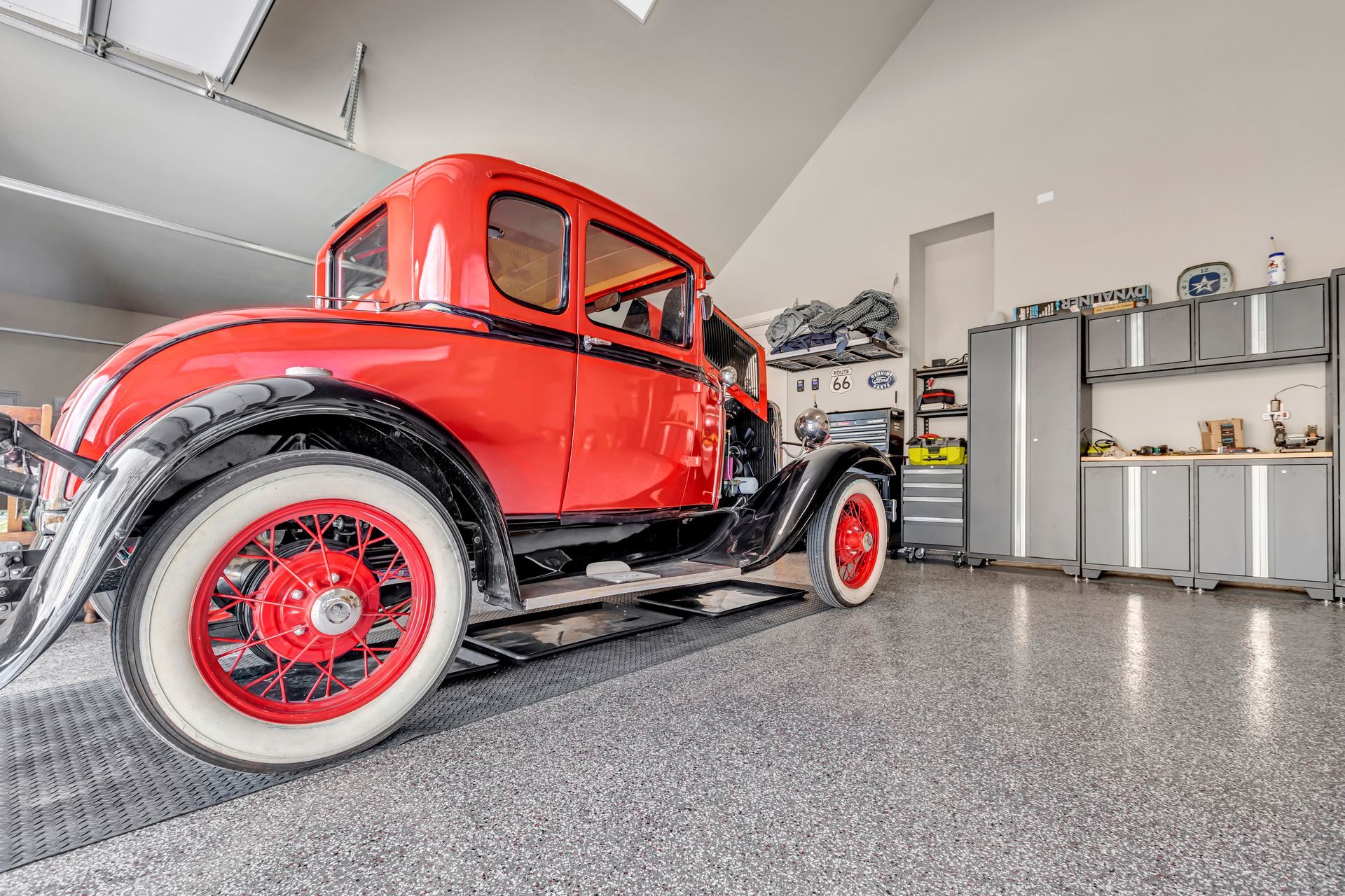 Red vintage car parked in a bright garage with polished gray floor and shelves in the background